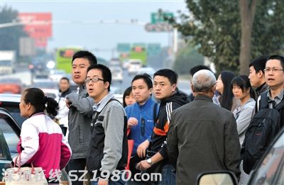 没挤上的乘客翘首企盼下一辆公交车的到来。